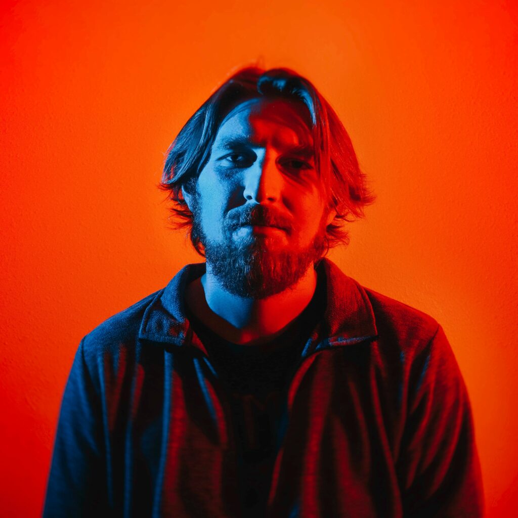 white man standing in front a the camera with red and blue lighting